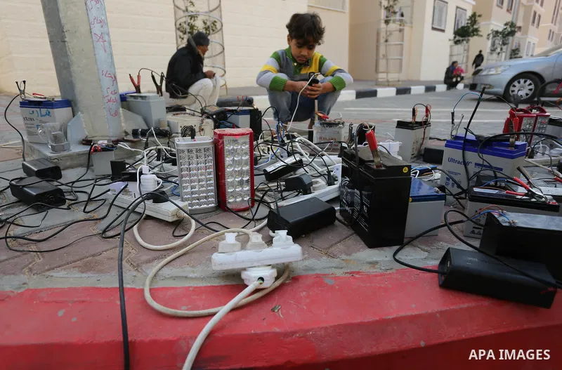 A Palestinian boy charges a mobile phone from batteries offered as a free service in his neighborhood which experiences power shortages, in Johr El-Deek in Gaza on February 1, 2018. Photo by Ashraf Amra
