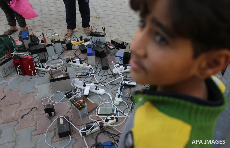 A Palestinian boy charges a mobile phone from batteries offered as a free service in his neighborhood which experiences power shortages, in Johr El-Deek in Gaza on February 1, 2018. Photo by Ashraf Amra