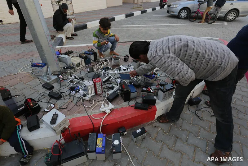 Palestinians charge their mobile phones from batteries offered as a free service in their neighborhood which experiences power shortages, in Johr El-Deek in Gaza on February 1, 2018. Photo by Ashraf Amra