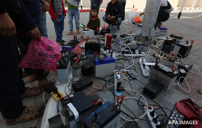 Palestinians charge their mobile phones from batteries offered as a free service in their neighborhood which experiences power shortages, in Johr El-Deek in Gaza on February 1, 2018. Photo by Ashraf Amra