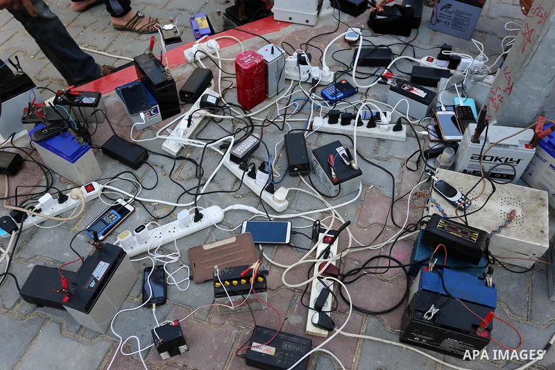 Palestinians charge their mobile phones from batteries offered as a free service in their neighborhood which experiences power shortages, in Johr El-Deek in Gaza on February 1, 2018. Photo by Ashraf Amra