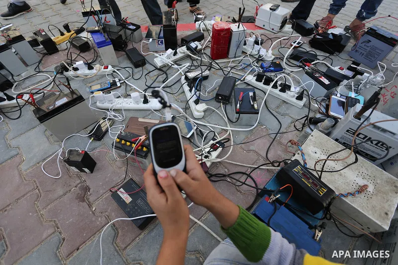 A Palestinian boy charges a mobile phone from batteries offered as a free service in his neighborhood which experiences power shortages, in Johr El-Deek in Gaza on February 1, 2018. Photo by Ashraf Amra