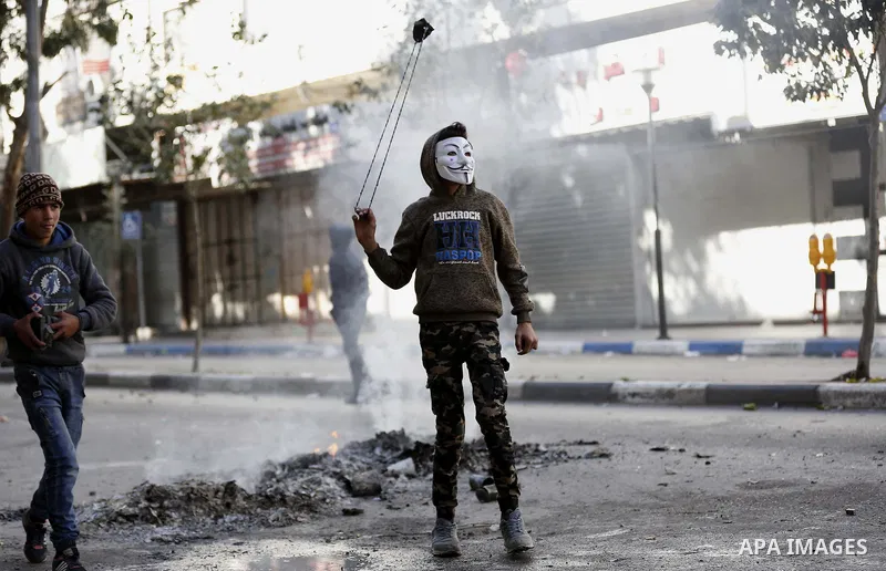 A masked Palestinian protester uses a slingshot to hurl stones towards Israeli security forces during clashes in the West Bank city of Hebron on February 2, 2018 2018 as demonstrations continue over the US president's co...