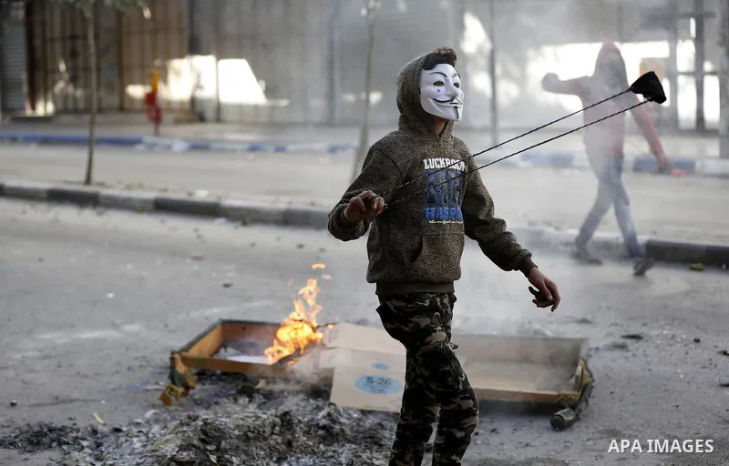 A masked Palestinian protester uses a slingshot to hurl stones towards Israeli security forces during clashes in the West Bank city of Hebron on February 2, 2018 2018 as demonstrations continue over the US president's co...