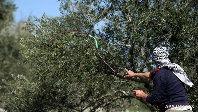 A Palestinian protester uses a slingshot to hurl stones towards Israeli security forces during clashes following a weekly demonstration against the expropriation of Palestinian land by Israel in the village of Kfar Qaddu...