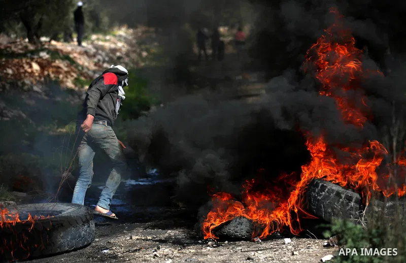 A Palestinian protester moves a burning tire during clashes with Israeli security forces following a weekly demonstration against the expropriation of Palestinian land by Israel in the village of Kfar Qaddum, near Nablus...