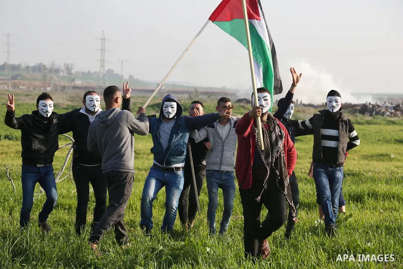 Palestinian demonstrators wearing Guy Fawkes' masks perform a traditional "dabke" dance with a Palestinian flag as a band performs during clashes near the border with Israel, east of Gaza City on February 2, 2018. Photo...