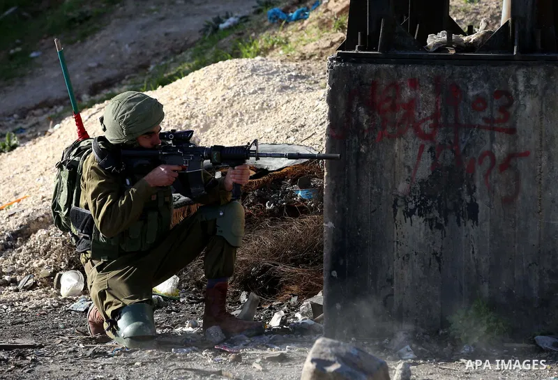 An Israeli soldier aims his weapon towards Palestinian protesters during clashes following a demonstration near the Hawara checkpoint, south of the West Bank city of Nablus on February 2, 2018, as demonstrations continue...