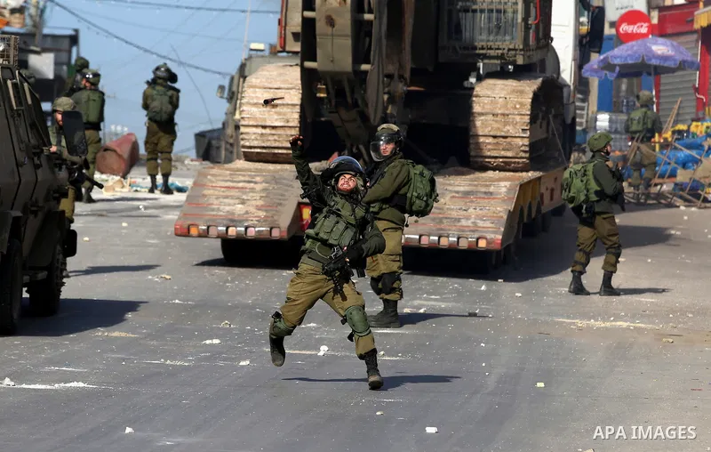 A member of Israeli security forces throws a tear gas canister towards Palestinian protesters during a search operation for Palestinians suspected of carrying out attacks in the West Bank village of Zababdeh, north of Je...