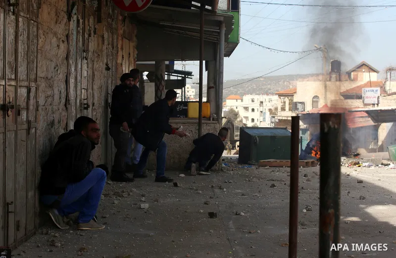 Palestinian protesters take cover form a tear gas canister fired by Israeli security forces during a search operation for Palestinians suspected of carrying out attacks in the West Bank village of Zababdeh, north of Jeni...