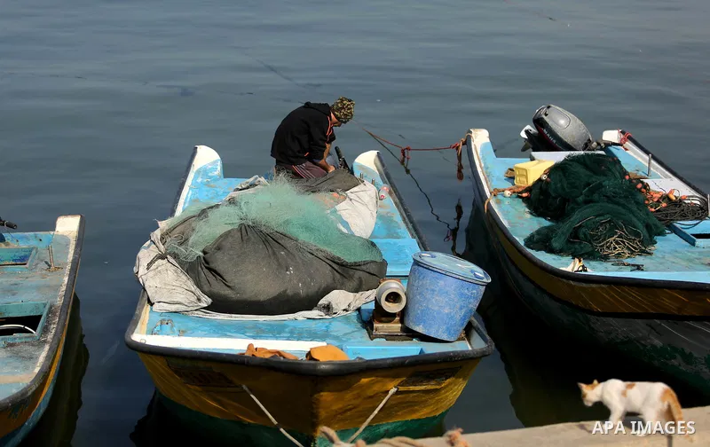 A Palestinian fisherman works on his fishing boat in Gaza sea port on February 3, 2018. Photo by Ashraf Amra