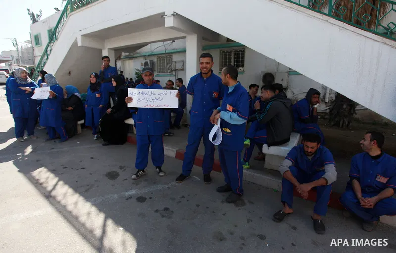 Palestinian cleaners hold banners during a protest to demand their salaries, at al-Shifa hospital in Gaza City on February 4, 2018. Photo by Mahmoud Ajour