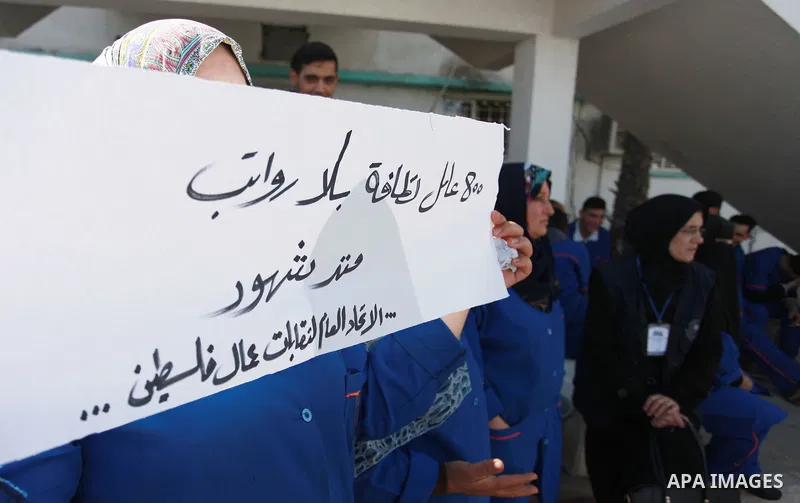 Palestinian cleaners hold banners during a protest to demand their salaries, at al-Shifa hospital in Gaza City on February 4, 2018. Photo by Mahmoud Ajour
