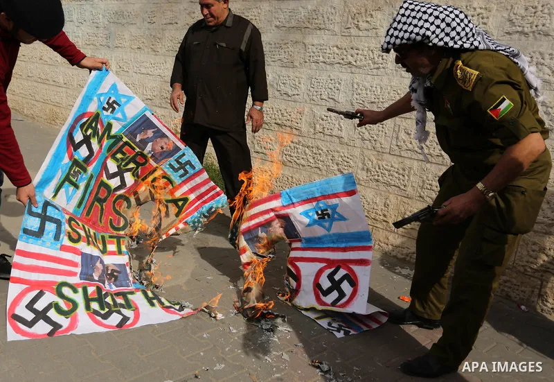 A Palestinian demonstrator burns posters depicting U.S. President Donald Trump, an Israeli, British and U.S. flags during a protest to show solidarity with Palestinian prisoners held in Israeli jails, in front of Red cro...