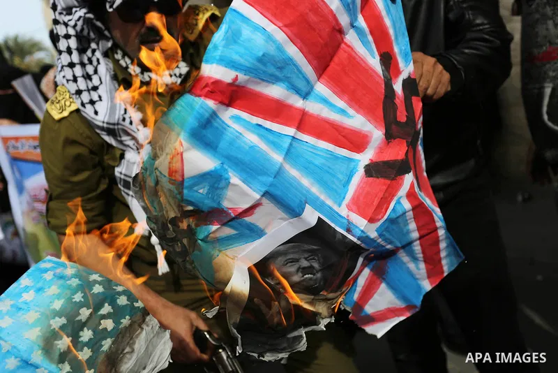 A Palestinian demonstrator burns posters depicting U.S. President Donald Trump, an Israeli, British and U.S. flags during a protest to show solidarity with Palestinian prisoners held in Israeli jails, in front of Red cro...