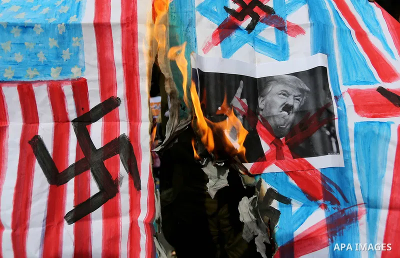 A Palestinian demonstrator burns posters depicting U.S. President Donald Trump, an Israeli, British and U.S. flags during a protest to show solidarity with Palestinian prisoners held in Israeli jails, in front of Red cro...