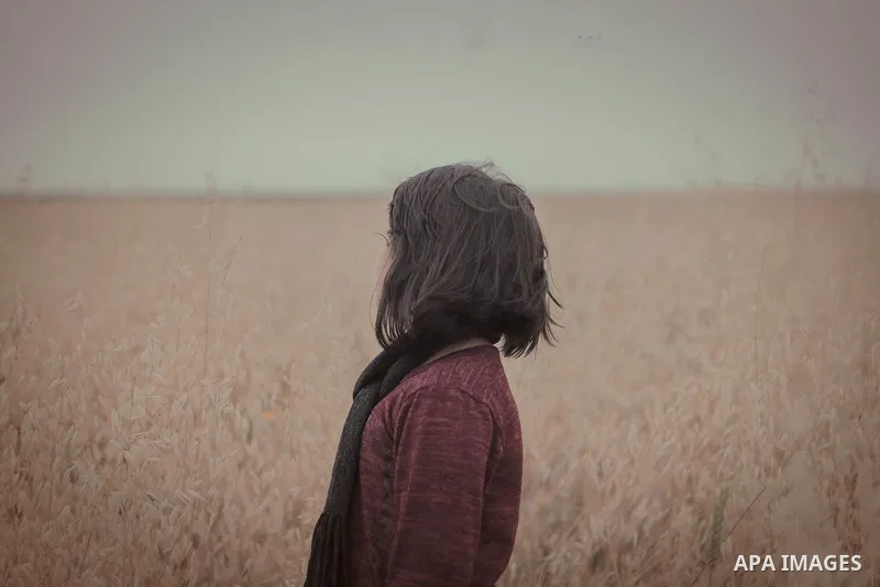 A young girl with wavy hair looks to grain field at sunset. Photo by Sanad Ltefa