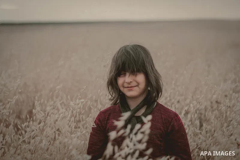 A young girl with smile standing in grain field at sunset. Photo by Sanad Ltefa