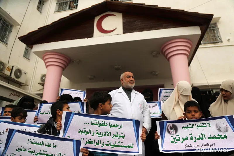 Palestinians hold placards during a protest outside Durra hospital in Gaza City after it stopped its services on February 7, 2018 after it ran out of fuel. Seven medical centers in Gaza have stopped services due to lack...