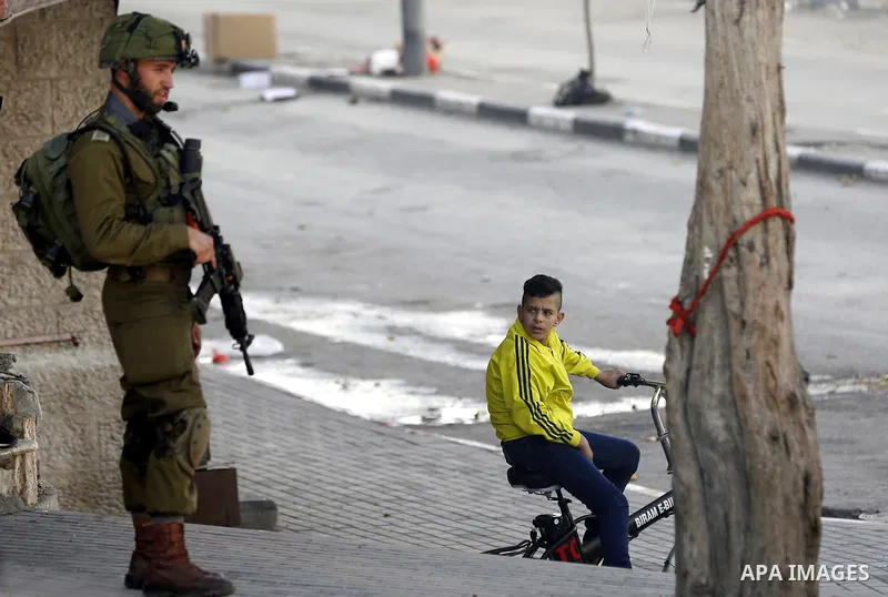 Palestinian youths ride their bicycles as Israeli security froces stand guard during clashes with Palestinian protesters as demonstrations continue over US President Donald Trump's declaration of Jerusalem as Israel's ca...
