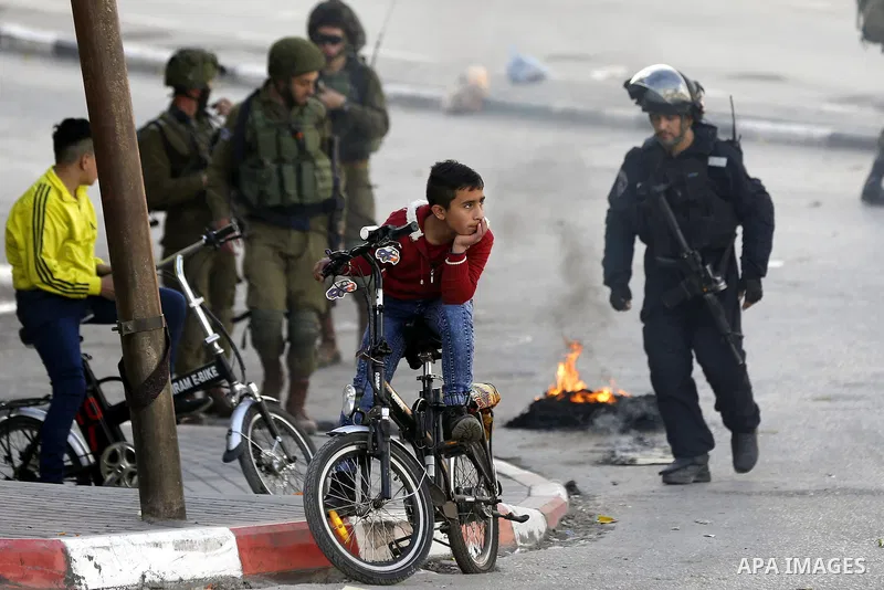 Palestinian youths ride their bicycles as Israeli security froces stand guard during clashes with Palestinian protesters as demonstrations continue over US President Donald Trump's declaration of Jerusalem as Israel's ca...