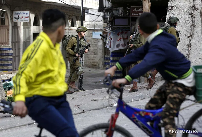 Palestinian youths ride their bicycles as Israeli security froces stand guard during clashes with Palestinian protesters as demonstrations continue over US President Donald Trump's declaration of Jerusalem as Israel's ca...