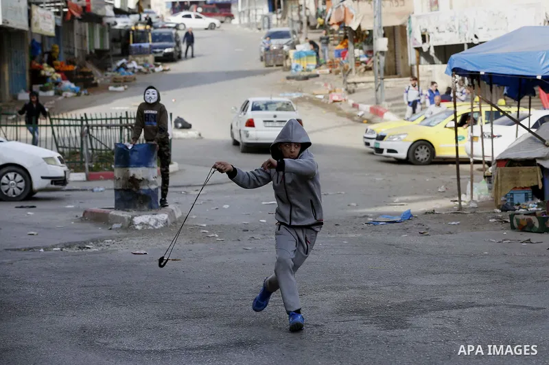 A Palestinian protester uses a slingshot to hurl stones towards Israeli security forces during clashes as demonstrations continue over US President Donald Trump's declaration of Jerusalem as Israel's capital, in the West...