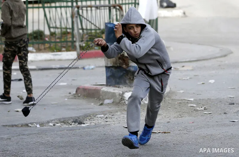 A Palestinian protester uses a slingshot to hurl stones towards Israeli security forces during clashes as demonstrations continue over US President Donald Trump's declaration of Jerusalem as Israel's capital, in the West...