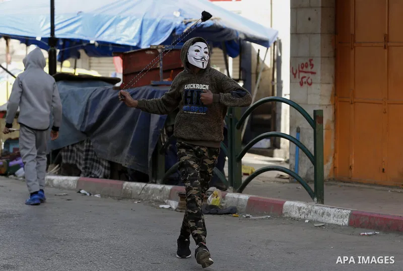 A Palestinian protester uses a slingshot to hurl stones towards Israeli security forces during clashes as demonstrations continue over US President Donald Trump's declaration of Jerusalem as Israel's capital, in the West...