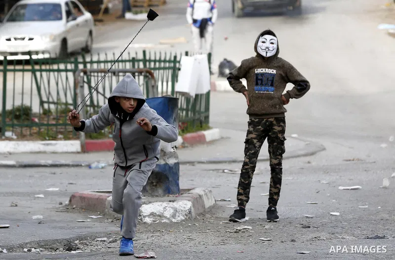 A Palestinian protester uses a slingshot to hurl stones towards Israeli security forces during clashes as demonstrations continue over US President Donald Trump's declaration of Jerusalem as Israel's capital, in the West...