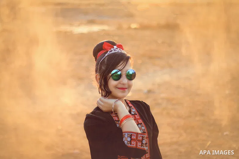 A girl wearing a traditional dress and glasses with a sweet smile. Photo by Sanad Ltefa