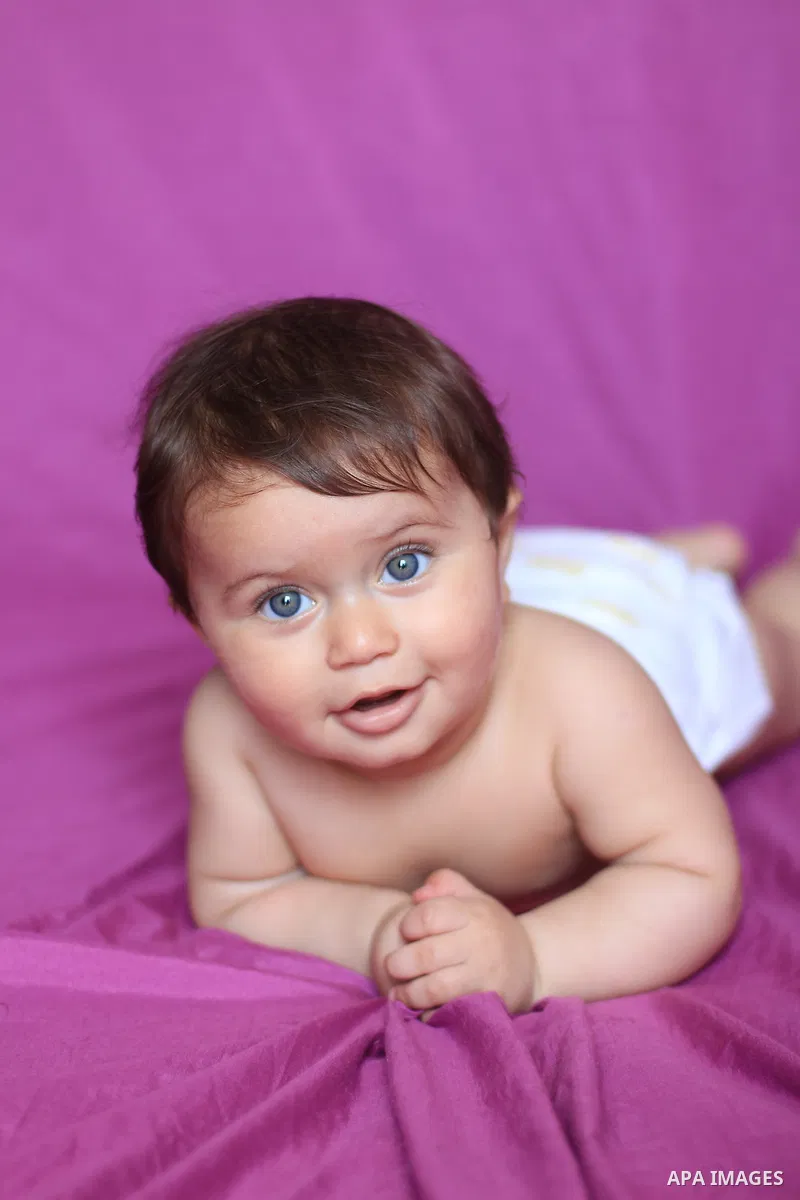 A baby smiles as he lies on his bed. Photo by Sanad Ltefa