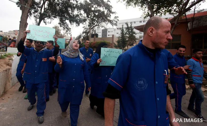 Palestinian cleaners hold banners during a protest to demand their salaries, at al-Shifa hospital in Gaza City on February 12, 2018. Photo by Mahmoud Ajour