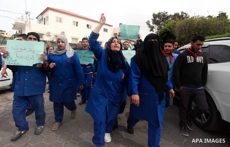 Palestinian cleaners hold banners during a protest to demand their salaries, at al-Shifa hospital in Gaza City on February 12, 2018. Photo by Mahmoud Ajour