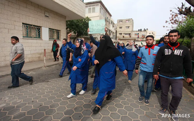 Palestinian cleaners hold banners during a protest to demand their salaries, at al-Shifa hospital in Gaza City on February 12, 2018. Photo by Mahmoud Ajour
