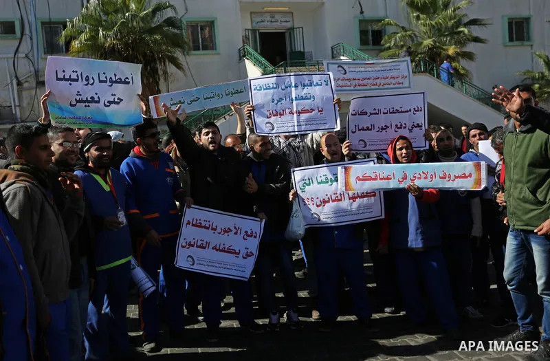 Palestinian cleaners hold banners during a protest to demand their salaries, at al-Shifa hospital in Gaza City on February 13, 2018. Photo by Ashraf Amra