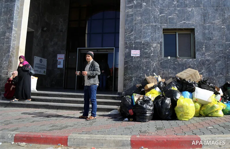 Palestinians stand near pile of waste during strike of Palestinian cleaners at al-Shifa hospital in Gaza City on February 13, 2018. Photo by Atia Darwish
