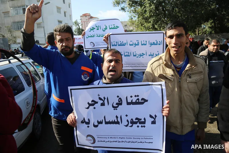 Palestinian cleaners hold banners during a protest to demand their salaries, at al-Shifa hospital in Gaza City on February 13, 2018. Photo by Atia Darwish
