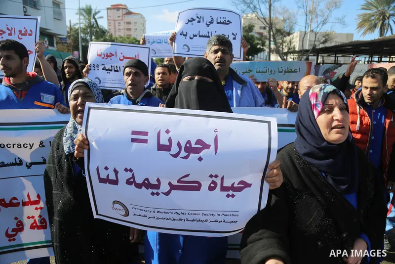 Palestinian cleaners hold banners during a protest to demand their salaries, at al-Shifa hospital in Gaza City on February 13, 2018. Photo by Atia Darwish
