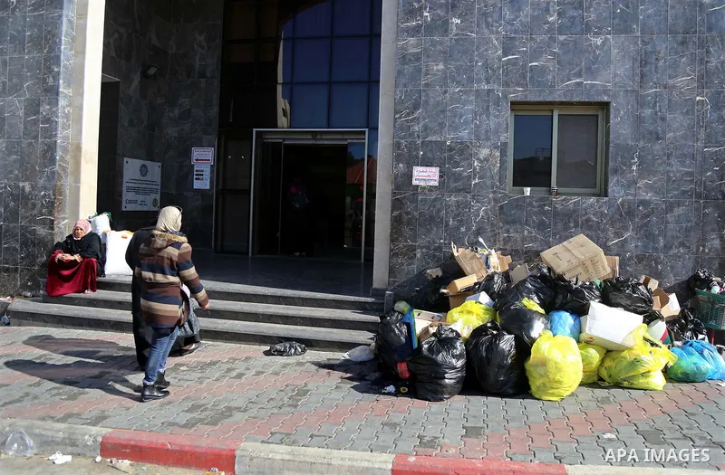 Palestinians stand near pile of waste during strike of Palestinian cleaners at al-Shifa hospital in Gaza City on February 13, 2018. Photo by Atia Darwish