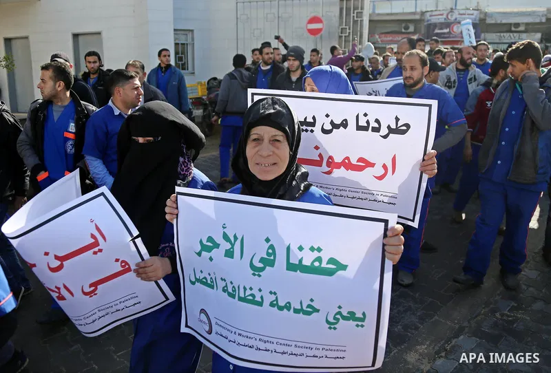 Palestinian cleaners hold banners during a protest to demand their salaries, at al-Shifa hospital in Gaza City on February 13, 2018. Photo by Atia Darwish