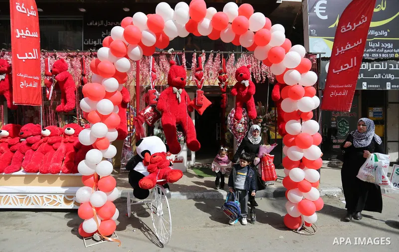 Palestinians walk past a shop selling red teddy bears, red ballons and pillows on Valentine's day in Gaza city on February 14, 2018. Valentine's Day is increasingly popular in the region as people have taken up the custo...