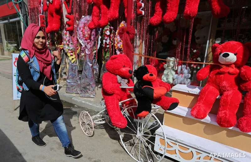 Palestinians walk past a shop selling red teddy bears, red ballons and pillows on Valentine's day in Gaza city on February 14, 2018. Valentine's Day is increasingly popular in the region as people have taken up the custo...