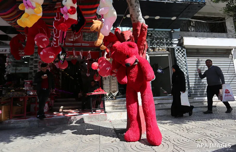 Palestinians walk past a shop selling red teddy bears, red ballons and pillows on Valentine's day in Gaza city on February 14, 2018. Valentine's Day is increasingly popular in the region as people have taken up the custo...