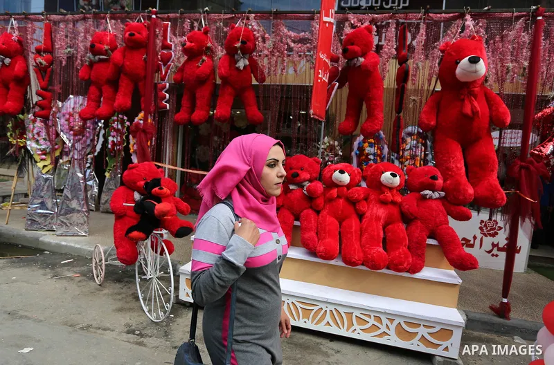 A Palestinian woman walks past a shop selling red teddy bears, red ballons and pillows on Valentine's day in Gaza city on February 14, 2018. Valentine's Day is increasingly popular in the region as people have taken up t...