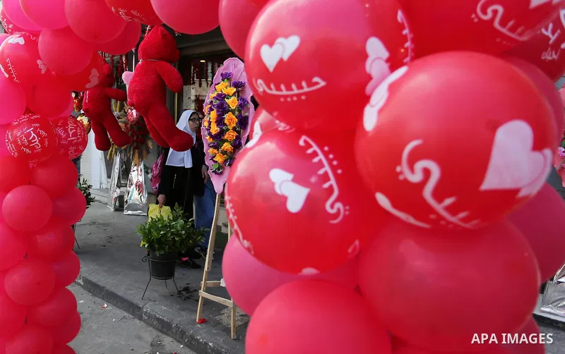 Palestinians walk past a shop selling red teddy bears, red ballons and pillows on Valentine's day in Gaza city on February 14, 2018. Valentine's Day is increasingly popular in the region as people have taken up the custo...