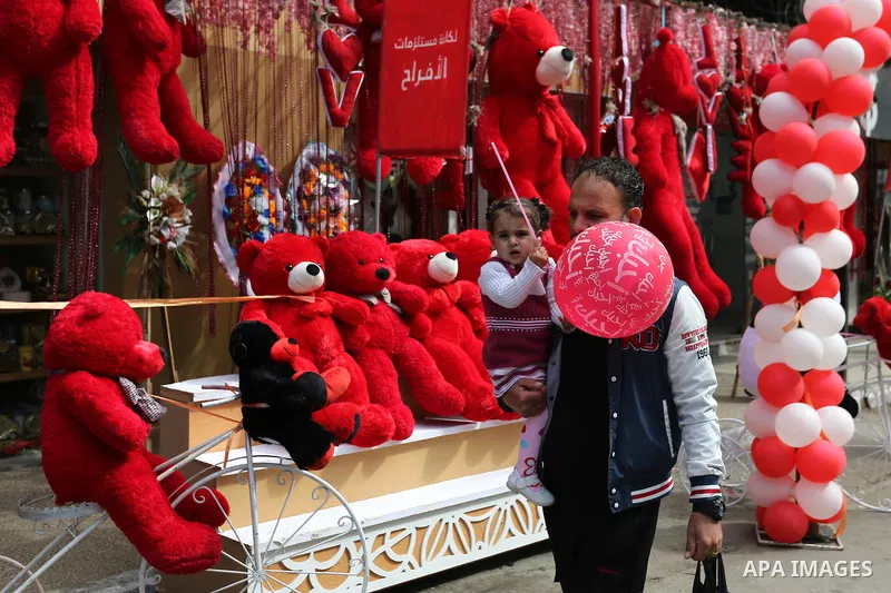 A Palestinian man walks past a shop selling red teddy bears, red ballons and pillows on Valentine's day in Gaza city on February 14, 2018. Valentine's Day is increasingly popular in the region as people have taken up the...