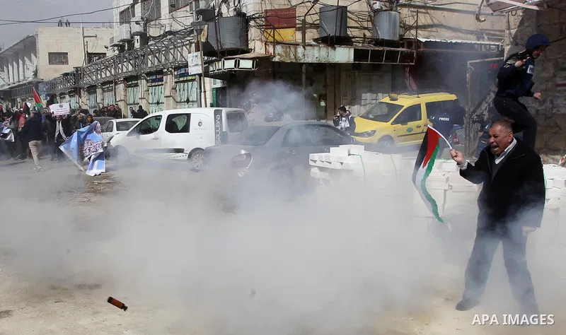 A Palestinian protester holds the national flag as tear gas is fired by Israeli troops during clashes following a demonstration demanding to dismantle the Ghetto, to mark the 24th anniversary of Ibrahimi mosque massacre...