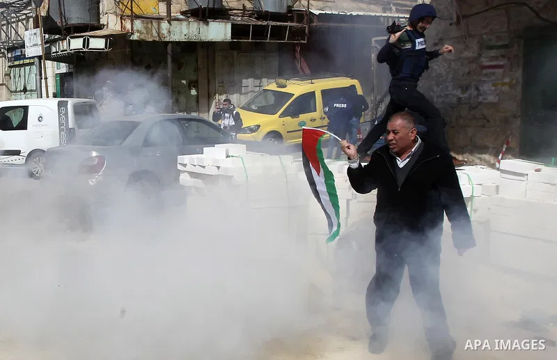 A Palestinian protester holds the national flag as tear gas is fired by Israeli troops during clashes following a demonstration demanding to dismantle the Ghetto, to mark the 24th anniversary of Ibrahimi mosque massacre...