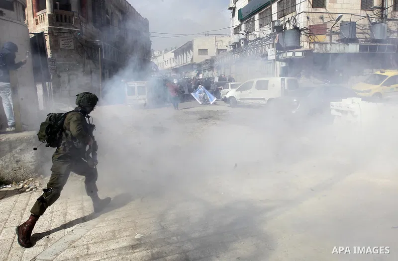 An Israeli soldier runs as tear gas is fired during clashes with Palestinian protesters following a demonstration demanding to dismantle the Ghetto, to mark the 24th anniversary of Ibrahimi mosque massacre when Baruch Go...